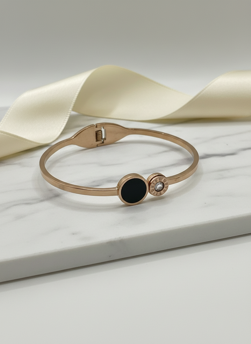 Rose gold bracelet with black gemstone and pearl on a white marble surface with beige ribbon
