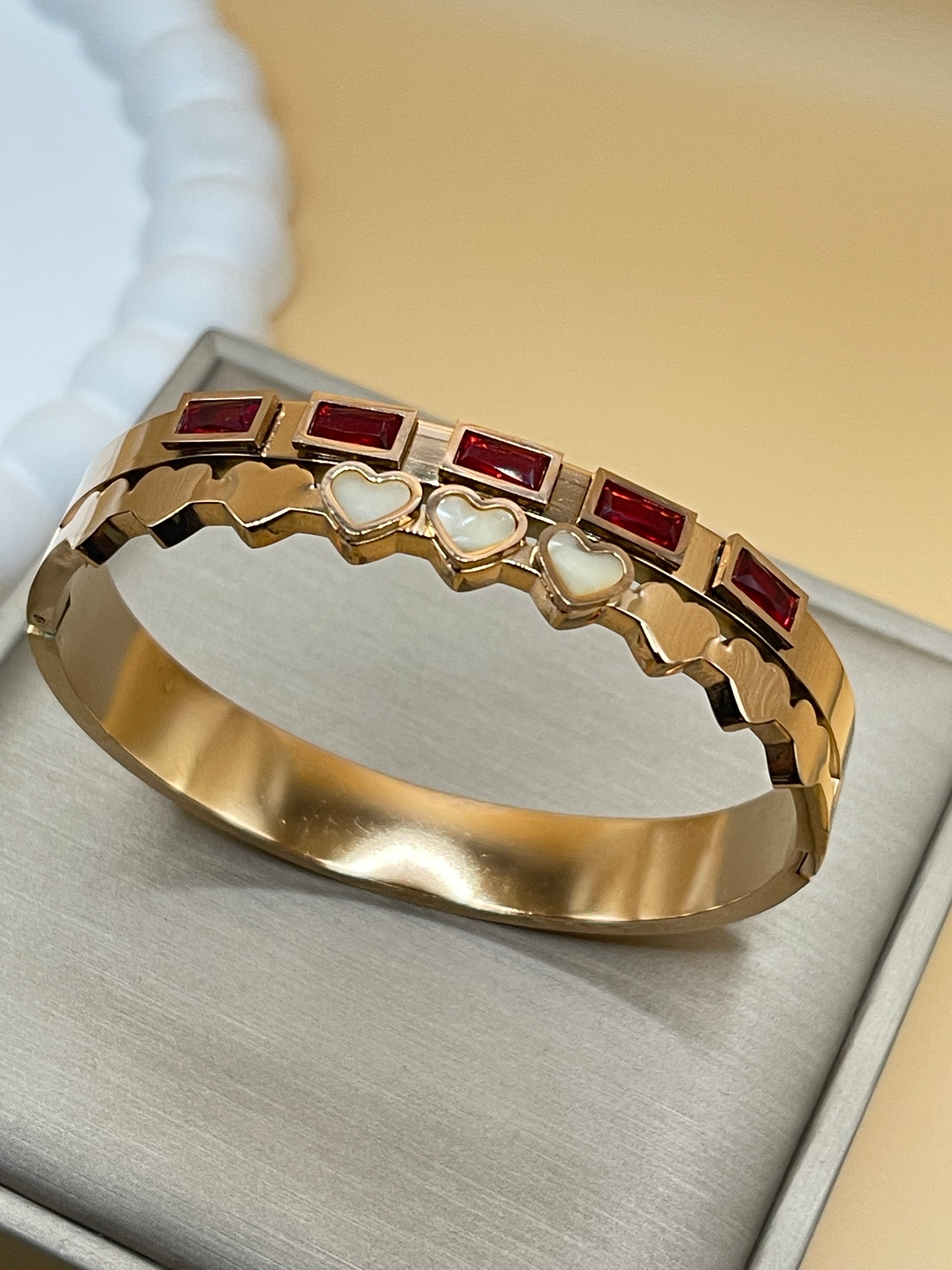 Rose gold bangle with red and white gemstones on a textured surface
