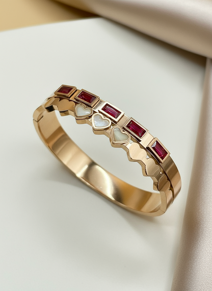 Rose gold bangle with embedded red gemstones on a light background