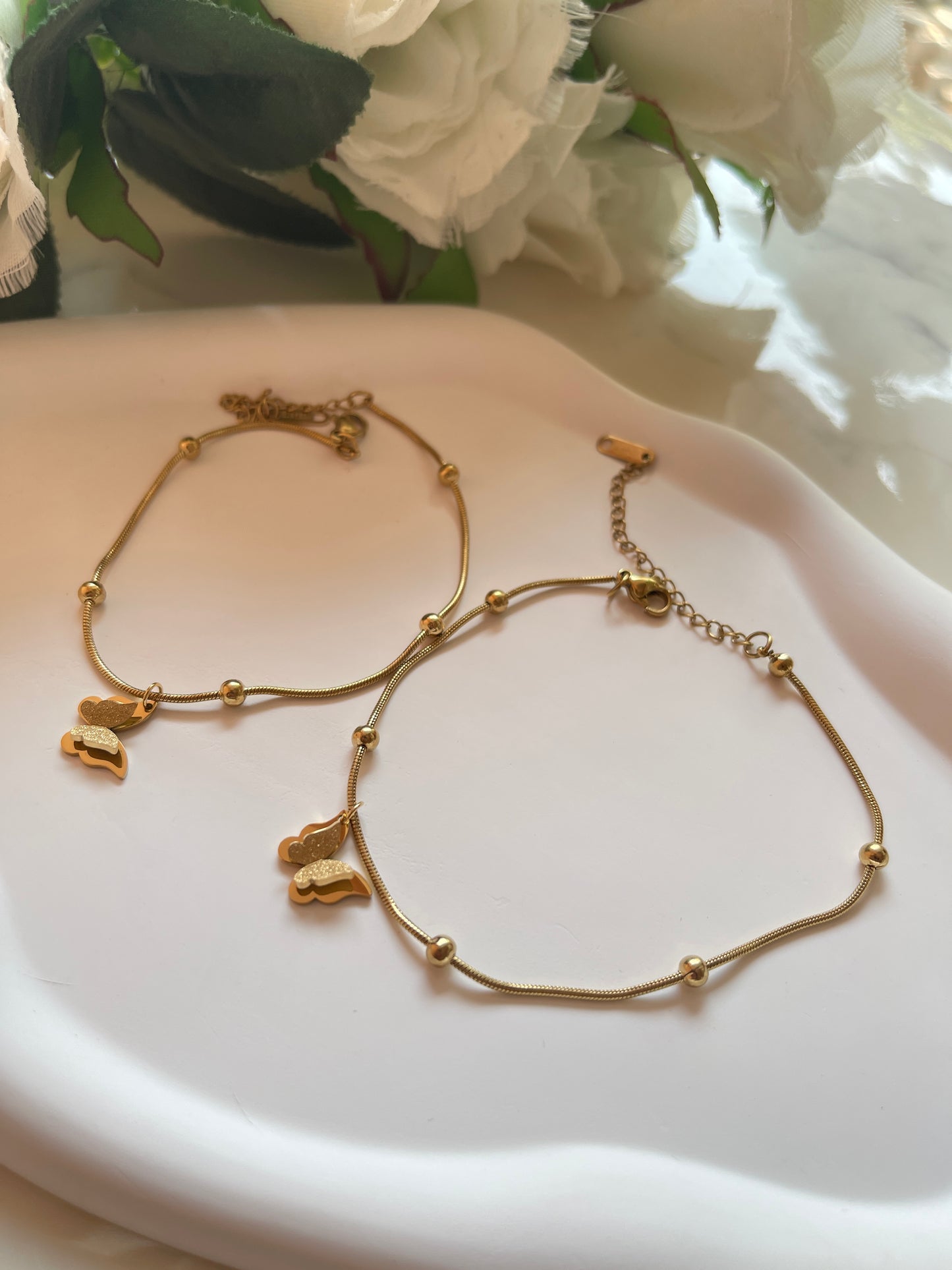 Gold bracelet with butterfly charms on a white dish with flowers in the background