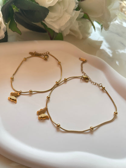 Gold bracelet with butterfly charms on a white dish with flowers in the background