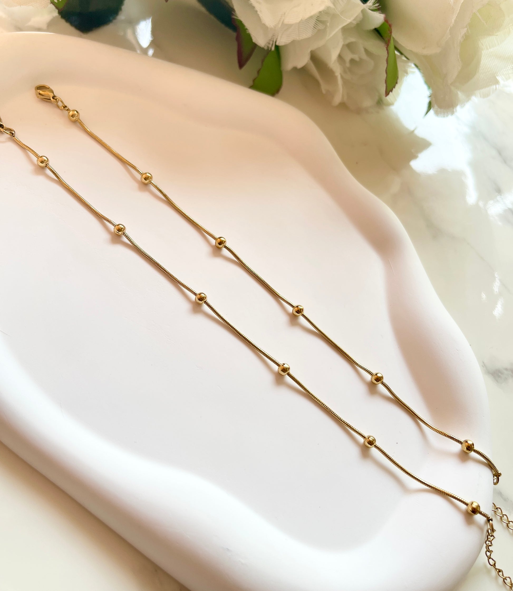 Gold necklace on a white surface with flowers in the background