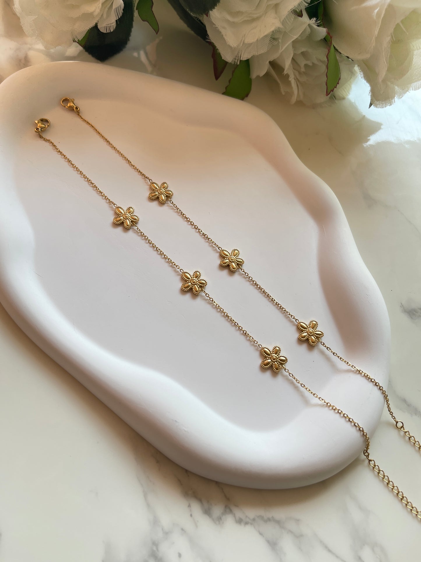Gold floral necklace on a white dish with white flowers in the background