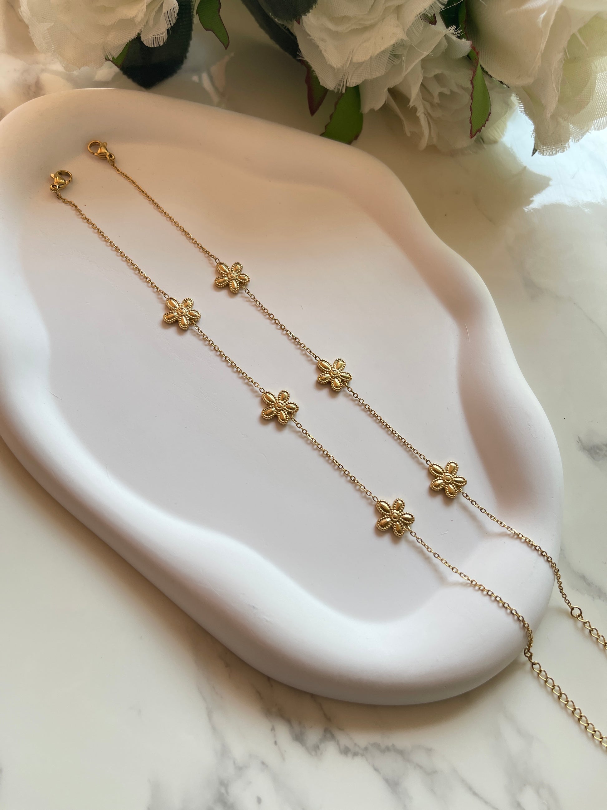 Gold floral necklace on a white dish with white flowers in the background