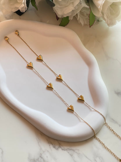 Gold heart-shaped necklace on a white dish with flowers in the background